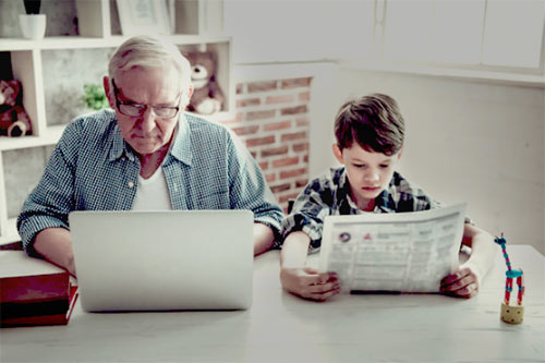 Elderly man on laptop, kid reading newspaper
